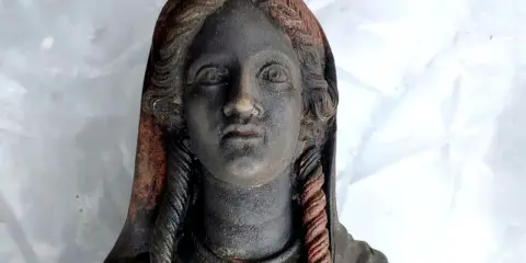Statua antica ritrovata nel santuario di San Casciano dei Bagni, con capelli intrecciati e volto enigmatico.