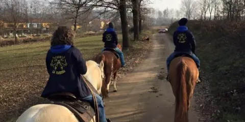 Cavalcata autunnale nei maneggi Piemonte, tre persone a cavallo su un sentiero sterrato tra alberi spogli e campi.