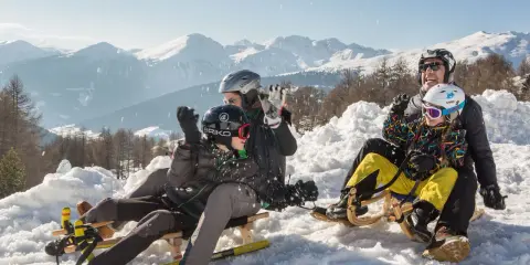 Famiglia felice in slittino sulla montagna per bambini in estate, con neve e montagne innevate sullo sfondo.
