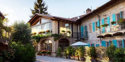 Un incantevole agriturismo in Piemonte, con un cortile acciottolato, balconi fioriti e persiane azzurre.