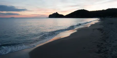 Tramonto sulla costa della Toscana, con un castello su una collina e il mare calmo. Un ricordo di vacanza con un neonato.