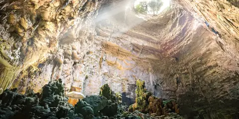 Grotta con stalattiti e stalagmiti illuminate da un raggio di sole. Un luogo magico da scoprire tra le cose da vedere vicino Alberobello.