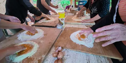 Bambini e adulti impastano farina e uova in una fattoria in Abruzzo, un'esperienza culinaria all'aperto.