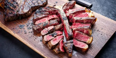 Una succulenta fiorentina alla griglia, affettata e servita su un tagliere di legno, con sale grosso sparso.