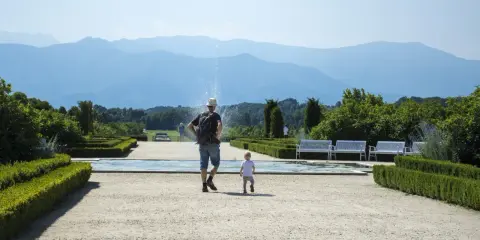 Un uomo e un bambino passeggiano in un giardino curato, con fontane e montagne sullo sfondo. Una giornata perfetta in Piemonte con bambini.