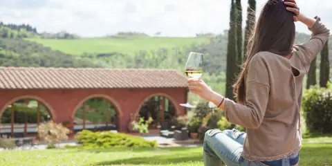 Donna con bicchiere di vino, vista su un casale con archi, paesaggio collinare. Un'oasi di pace tra gli agriturismi particolari Lombardia.