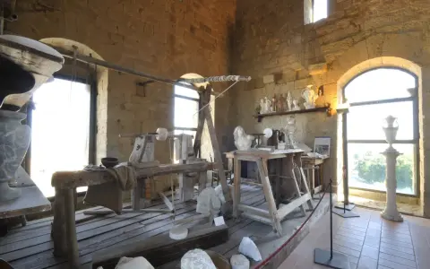 Laboratorio di scultura con attrezzi antichi e statue in marmo, che evoca la tradizione dell'alabastro toscana.