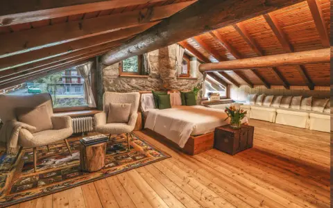 Accogliente camera con camino, travi in legno a vista, letto comodo, poltrone soffici e un tappeto decorato.