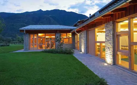 Edificio moderno con pietra e legno, circondato da prati verdi, con ampie vetrate che illuminano l'interno. Sembra un luogo ideale per fattorie con ristorante.