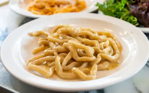 Pici cacio e pepe, un classico tra i piatti tipici di Siena, serviti su un piatto bianco.