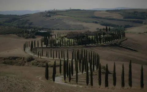 Un casale nel Val d'Orcia autunno, circondato da cipressi che disegnano curve sinuose su dolci colline.