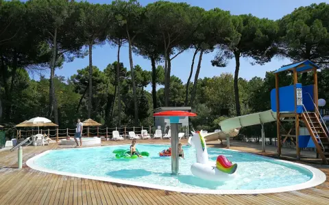 Bambini felici in piscina con gonfiabili, scivoli e giochi d'acqua. Perfetti campeggi Emilia Romagna per bambini, un'oasi di divertimento sotto i pini.