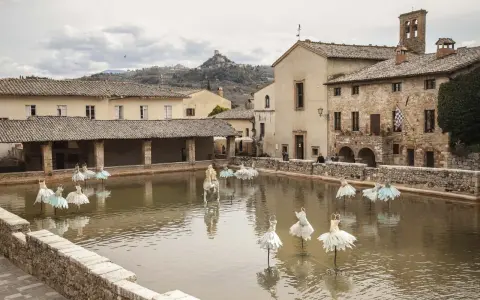 Bagno Vignoni: cosa vedere? La vasca termale con installazioni artistiche di abiti da ballo e un cavallo bianco.