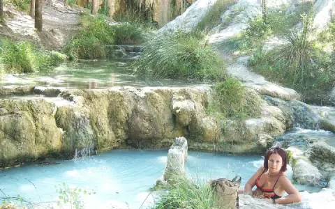 Donna rilassata nelle acque termali di Borgo San Filippo, tra rocce calcaree e vegetazione lussureggiante.
