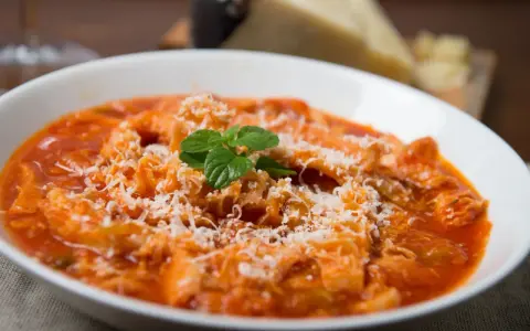 Trippa alla romana, uno dei piatti tipici del Lazio, servita in una ciotola bianca con parmigiano grattugiato e una fogliolina di menta.