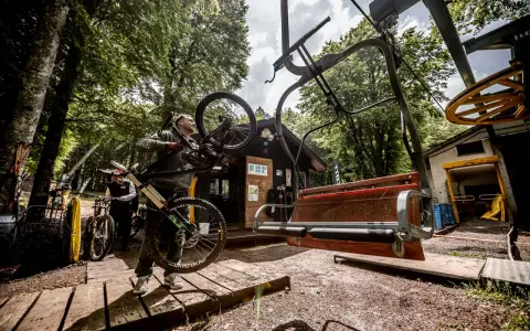 Ciclista porta la sua bici verso gli impianti di risalita ad Amiata, pronto per un'avventura in mountain bike.