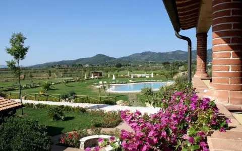 Un angolo di campagna toscana lungo il mare, con piscina, giardini curati e colline verdi all'orizzonte.
