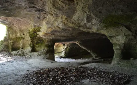 L'interno di una grotta scavata nella roccia, con nicchie e passaggi che ricordano Vitozza, la città perduta.
