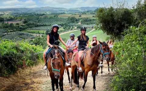 Un gruppo di amici si gode una **passeggiata a cavallo toscana** tra colline verdi e vigneti. Sorridono felici, immersi nella bellezza del paesaggio.