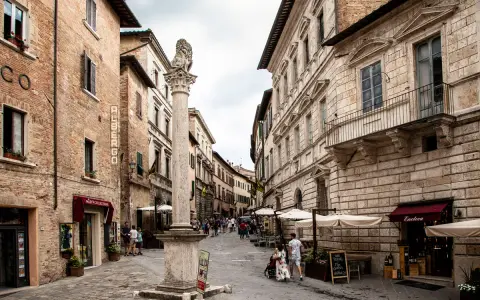 Un vicolo pittoresco tra i borghi vicino Montepulciano, con edifici storici, un leone scolpito su una colonna e tavolini all'aperto.