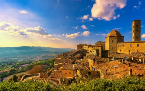 Un borgo toscano al tramonto, con tetti in cotto e un campanile svettante. Curiosità sulla Toscana: questo paesaggio evoca storie antiche.