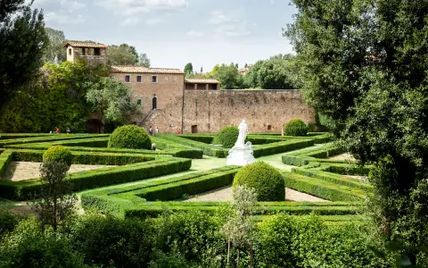Giardino all'italiana con siepi geometriche, una statua bianca e un antico borgo toscano da visitare sullo sfondo.