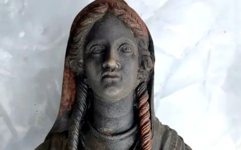 Statua antica ritrovata nel santuario di San Casciano dei Bagni, con capelli intrecciati e volto enigmatico.