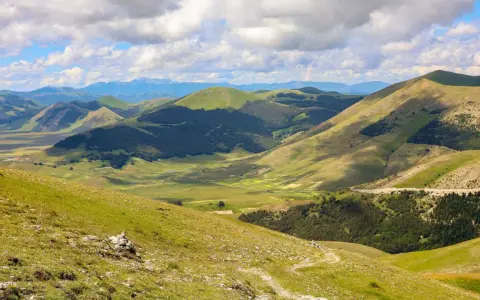 Panoramica dei Monti Sibillini, un paesaggio verdeggiante con dolci colline e valli, ideale per scoprire cosa vedere in questa zona.