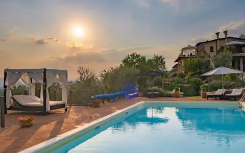 Piscina con lettini e gazebo, ideale per sapere dove dormire in Toscana. Tramonto suggestivo su un casale.