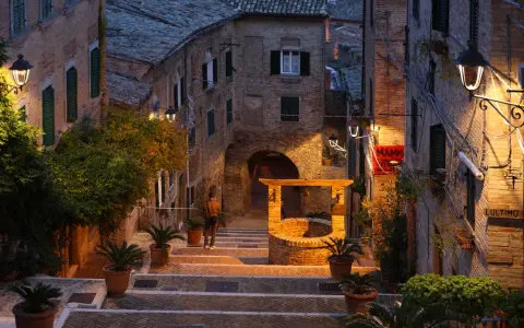 Un vicolo suggestivo a Montefeltro, cosa vedere: un pozzo antico, scalinate in pietra e luci soffuse creano un'atmosfera magica.