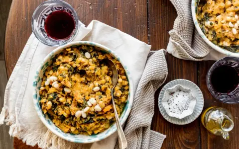 Un piatto fumante di fagioli e verdure, un classico delle ricette toscane, accompagnato da vino rosso e olio d'oliva.