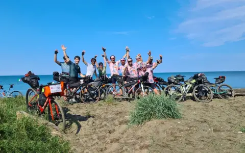 Un gruppo di ciclisti festeggia sulla spiaggia, pronti per un'avventura di cicloturismo in Toscana.