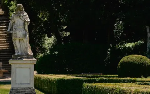 Statua romana domina la scalinata nei **Horti Leonini**. Giardini curati e alberi ombrosi creano un'atmosfera regale.