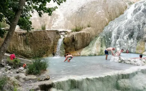 Persone si rilassano nelle piscine termali naturali di Castiglione d'Orcia, con cascate che scendono da rocce bianche.