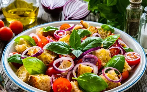 Panzanella ricetta: un'insalata estiva con pane raffermo, pomodorini, cipolla rossa e basilico fresco, condita con olio d'oliva.