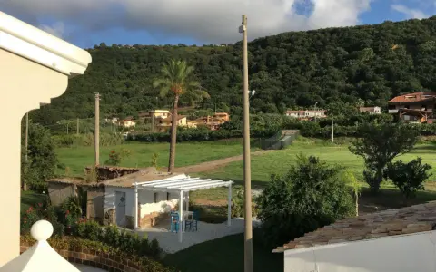 Un angolo di pace tra gli agriturismi in Calabria. Un pergolato bianco con tavolino e sedie blu, circondato da verde e colline rigogliose.
