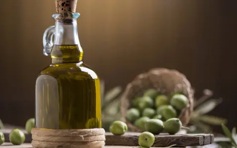 Bottiglia di olio extravergine di oliva, con olive verdi in cestino e su tagliere. La differenza tra olio di oliva e extravergine è la qualità.