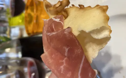 Fetta di gnocco fritto con prosciutto crudo, un classico dei piatti tipici Parma, accompagnato da vino rosso.