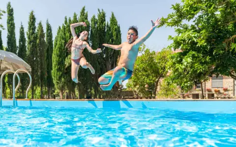 Bambini che saltano in piscina, una gioiosa Pasqua in Toscana tra cipressi e sole.