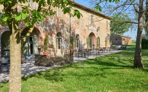 Antica locanda nel Val di Chiana, con tavoli all'aperto e un prato fiorito.