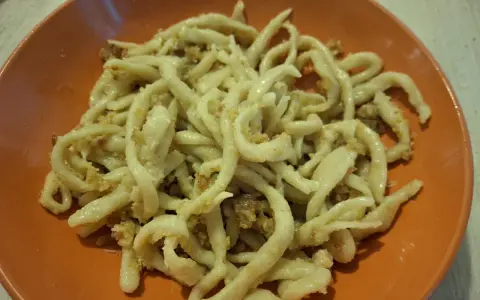 Pici fatti in casa con un saporito sugo per i pici, serviti in un piatto arancione.