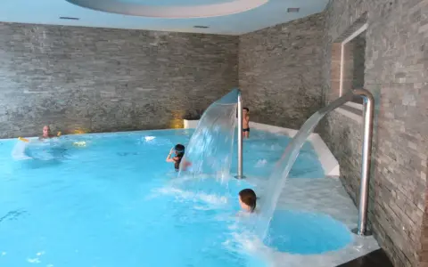 Bambini si divertono sotto cascate d'acqua in una piscina interna, un'ottima spa per famiglie in Lombardia.