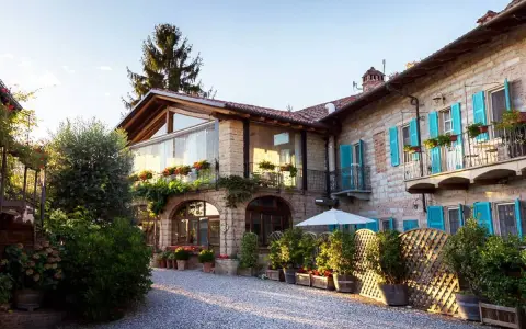 Un incantevole agriturismo in Piemonte, con un cortile acciottolato, balconi fioriti e persiane azzurre.