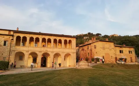 Edificio storico con portico ad archi, un pozzo e persone che passeggiano. Un luogo che sembra uscito da uno dei tanti film girati a Montepulciano.
