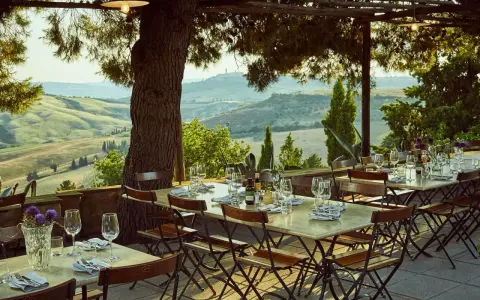Tavoli apparecchiati sotto un pergolato con vista sulle colline toscane. Un'atmosfera perfetta per gustare i sapori degli agriturismi in Toscana.