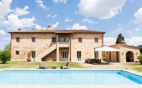 Splendida villa in pietra con piscina, un sogno di masserie toscane sotto un cielo azzurro.