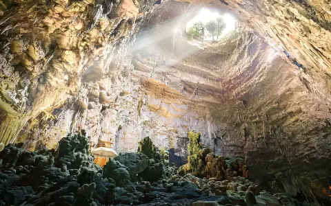 Grotta con stalattiti e stalagmiti illuminate da un raggio di sole. Un luogo magico da scoprire tra le cose da vedere vicino Alberobello.