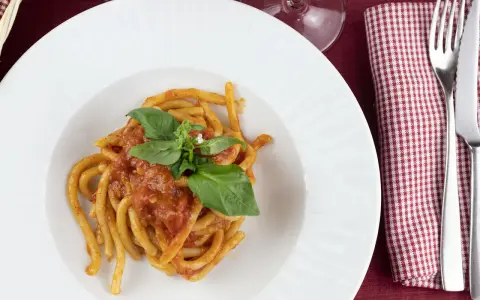 Pici al sugo, un classico della ricetta aglione Val di Chiana, serviti su un piatto bianco con basilico fresco.