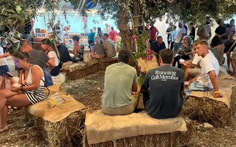 Gente seduta su balle di fieno sotto alberi, un evento estivo in Sicilia.