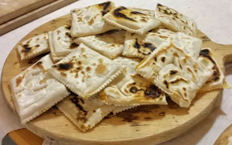 Piatto tipico cesenate: piadina fritta, dorata e leggermente bruciacchiata, servita su un tagliere di legno.